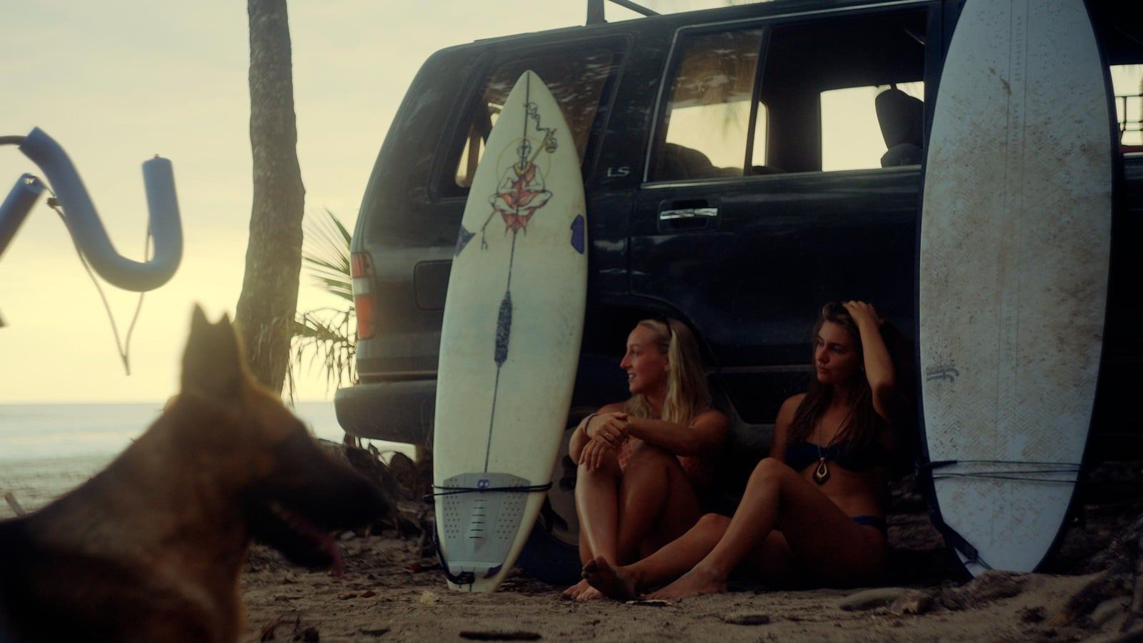 Surfboard leaning against a car while friends sit in the shade